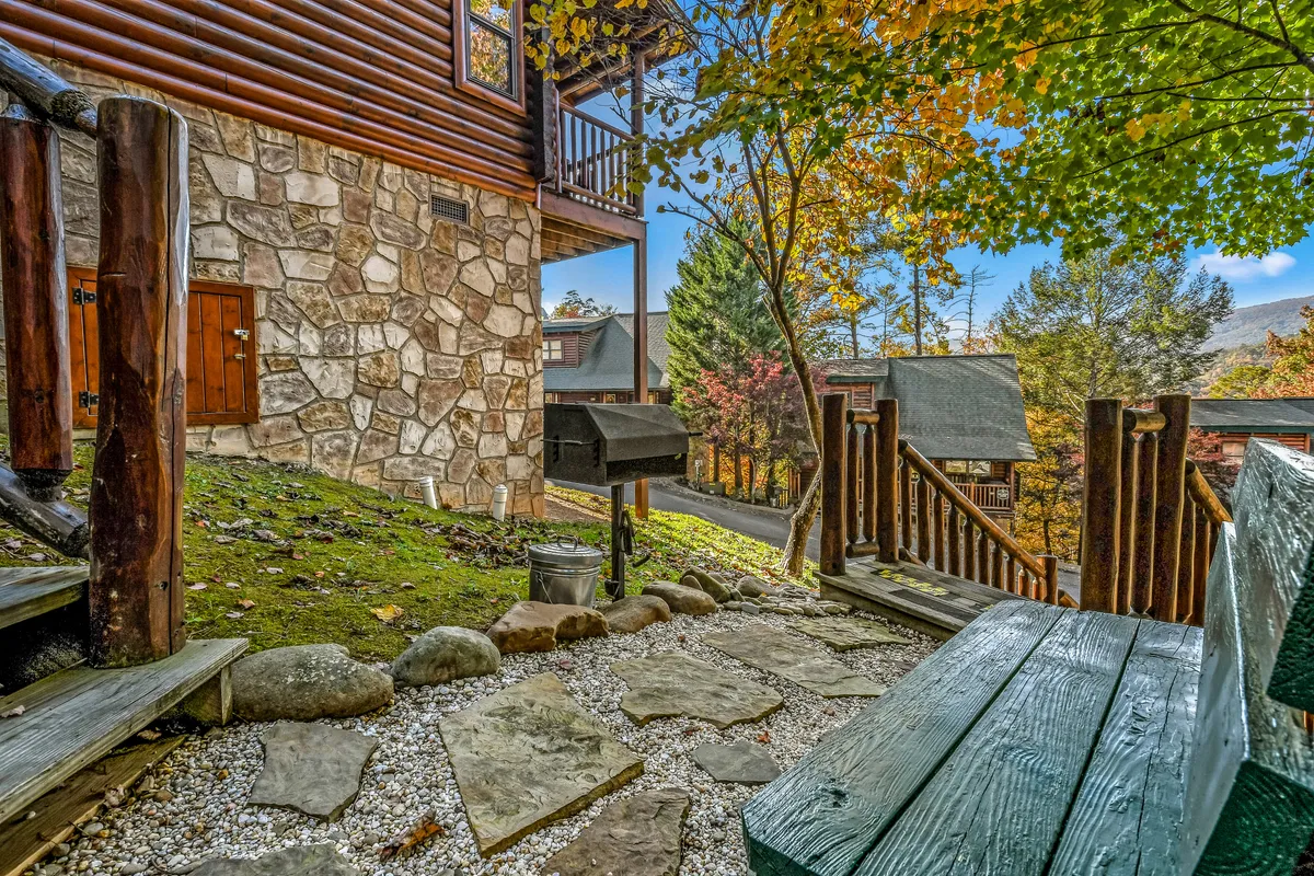 An exterior shot showing a stone wall, outdoor grill, wooden bench, and steps leading up, set against a cozy natural backdrop—perfect for alfresco barbecues and outdoor gatherings.