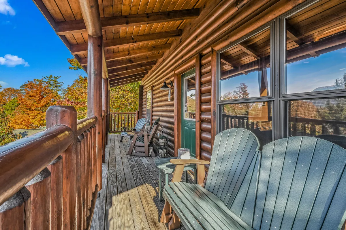 This exterior image features a classic wooden log cabin with inviting green Adirondack chairs and decorative lanterns, surrounded by beautiful autumn foliage. The cozy porch setting invites relaxation and small gatherings, while the warm golden light suggests a peaceful, private getaway.