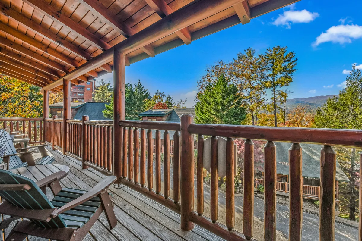 This image captures a tranquil cabin deck with wooden railings and classic rocking chairs overlooking distant mountains, framed by colorful autumn foliage. The setting is both serene and inviting, offering a place to relax after a day of adventure.