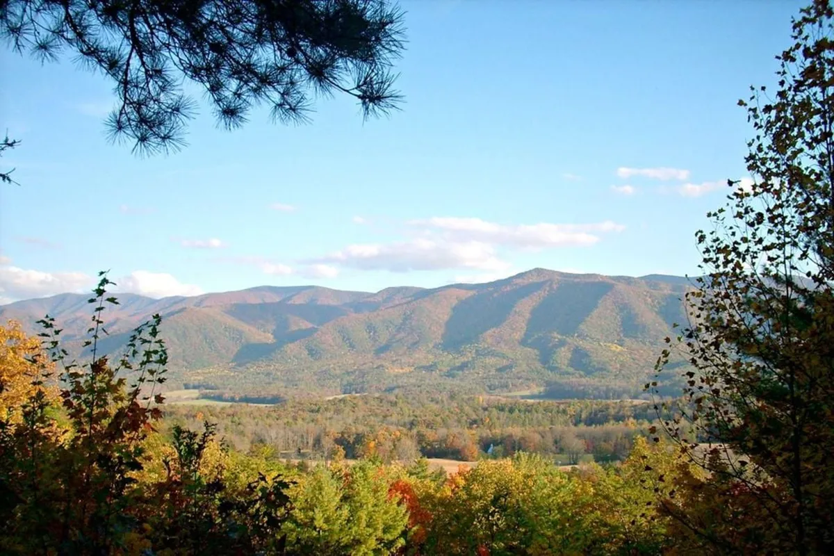 A sweeping view of the Smoky Mountains with autumn foliage and rolling clouds, evoking the grandeur and tranquility of the nearby national park. The scene invites thoughts of hiking, picnicking, and scenic bonding moments in nature.