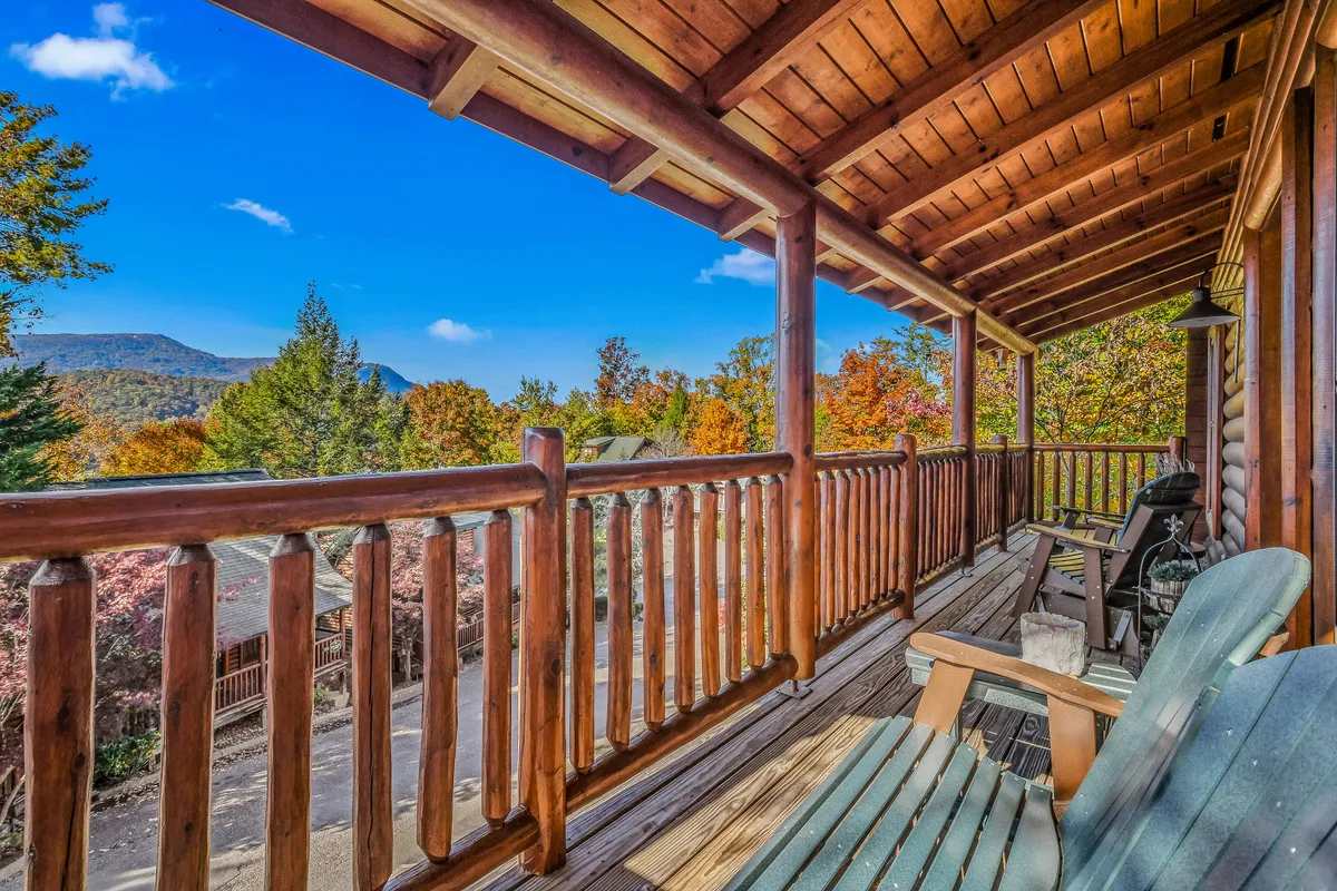 This image showcases a spacious wooden deck with log railings, two classic rocking chairs, and spectacular views of Buff Mountain and vibrant autumn trees. The serene setting is bathed in natural light, inviting guests to immerse themselves in the tranquil mountain atmosphere.