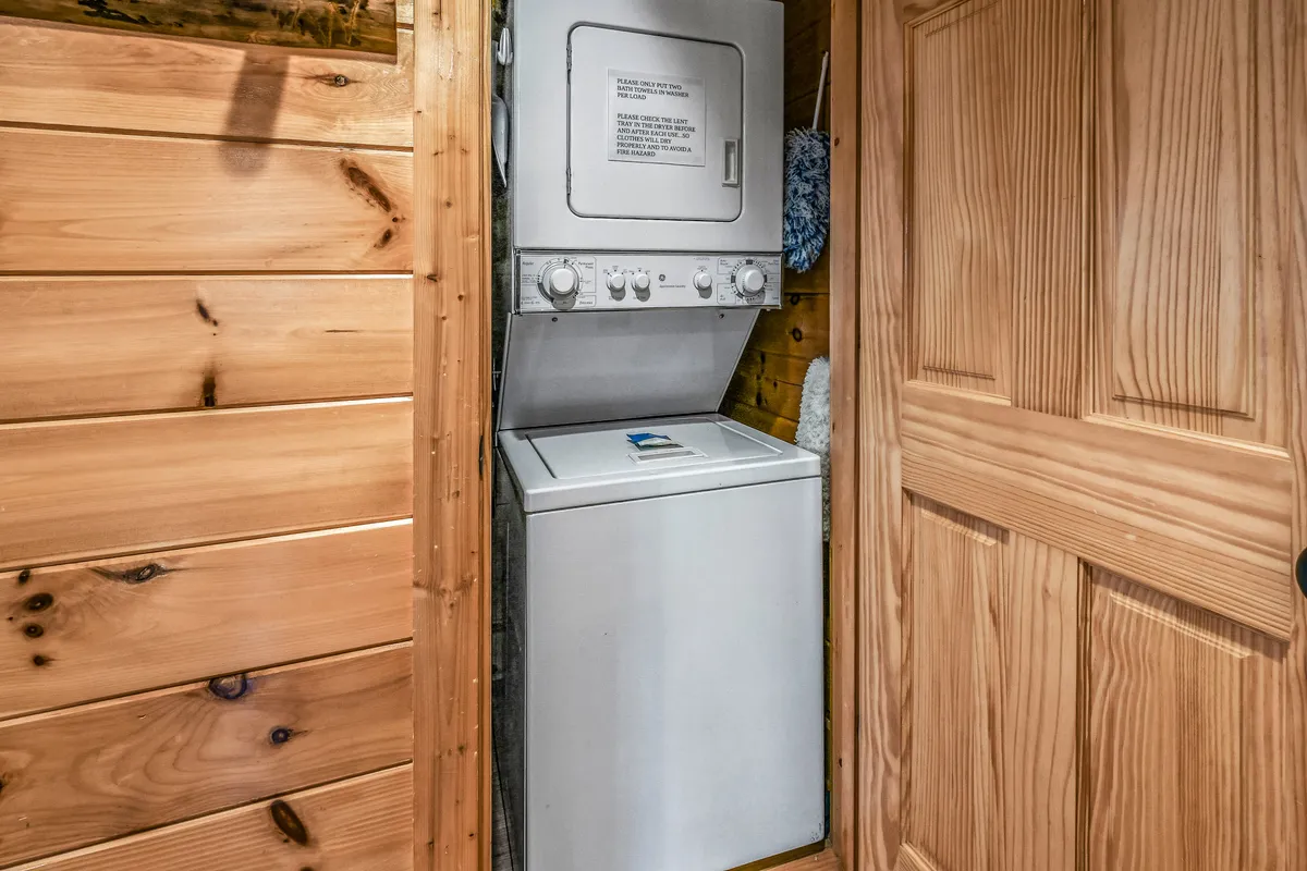 A practical yet welcoming view of the laundry area, featuring a stackable washer and dryer against wooden paneling, blending function with the cabin’s signature rustic style.