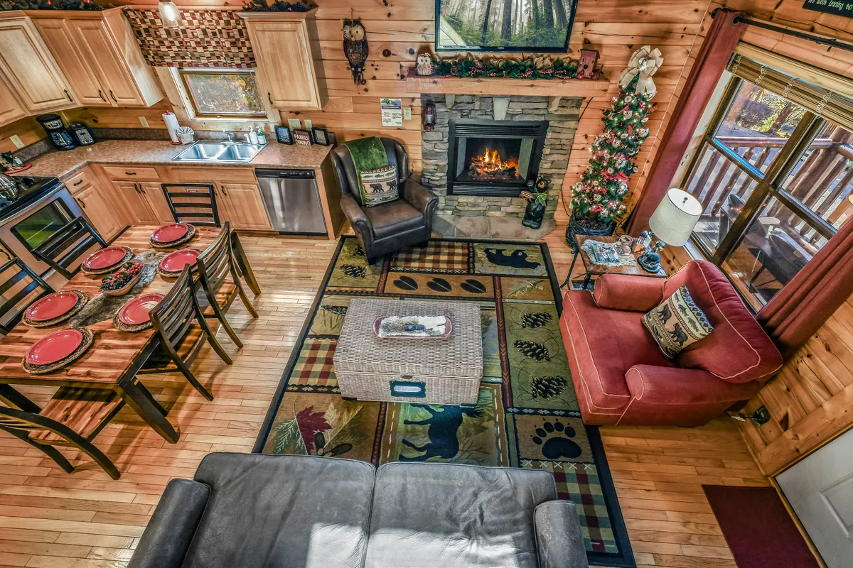 A warm, inviting shot featuring the kitchen with modern appliances, the dining table set for a family meal, a comfortable living room seating area, and festive touches like a Christmas tree by the window.