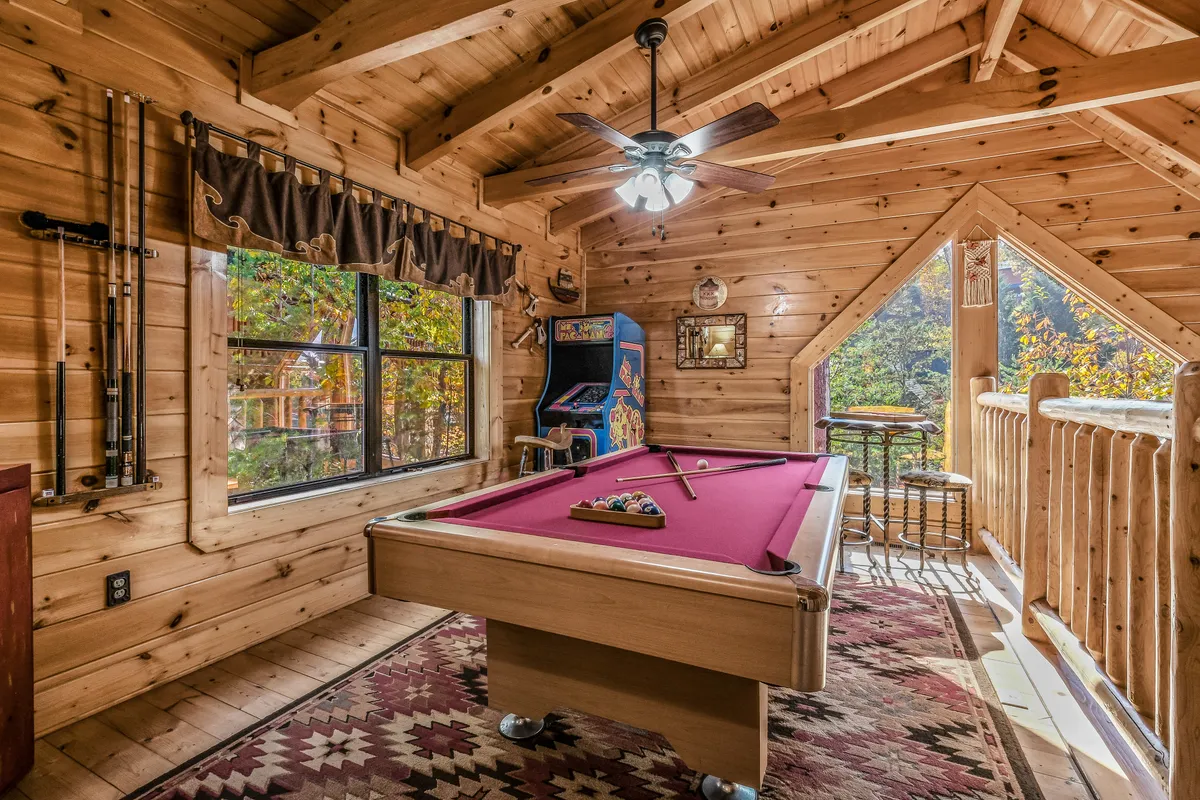 A bright loft space featuring a classic pool table as the central focus. Large windows flood the room with natural light, and an iconic Pac-Man arcade machine stands nearby, inviting friendly competition. The area is furnished with casual seating, creating a comfortable and playful retreat for guests.