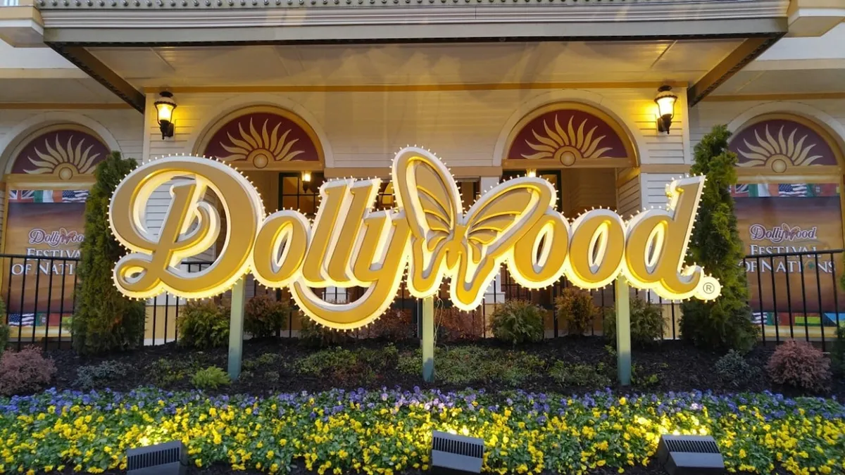 This image features the welcoming entrance sign to Dollywood, surrounded by vibrant flower beds and festive decorative lighting, setting the scene for a lively amusement park experience. Families are drawn to the inviting atmosphere that promises fun and shared memories.